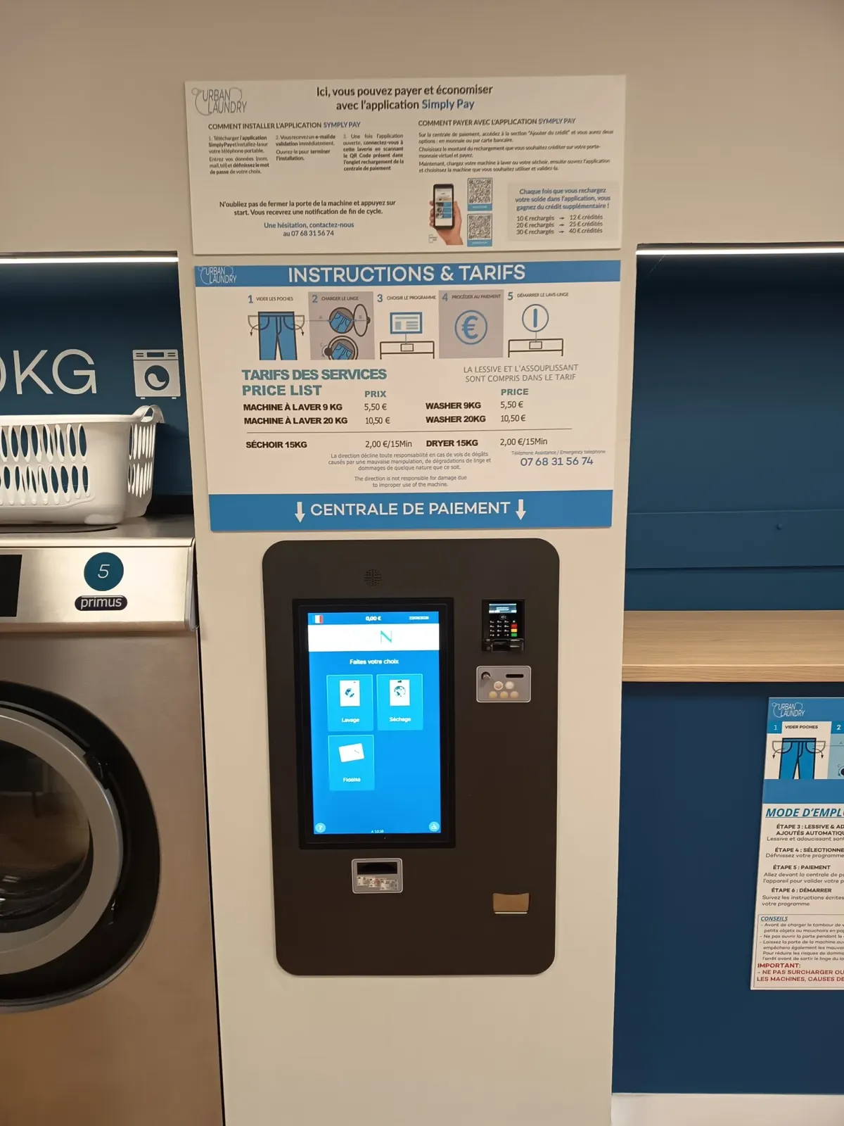 Borne de paiement centrale de la laverie avec l'affiche des instructions et tarifs