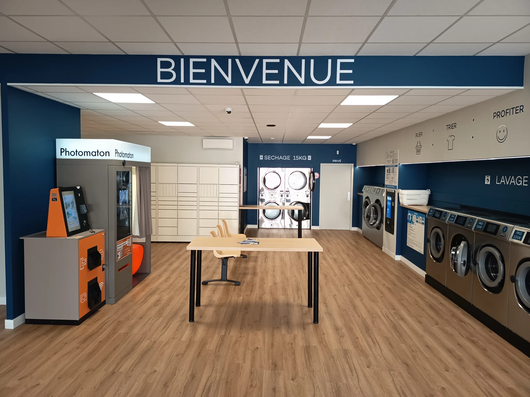 Salle de la laverie Urban Laundry à Toulouse Borderouge avec l'enseigne Bienvenue, le photomaton, les lave-linge et la table de pliage